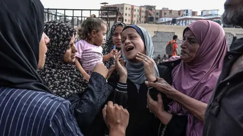 Getty Images A group of women comfort another woman in the middle of their group in Khan Yunis. 