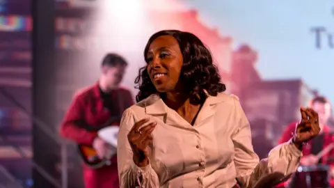 Graham Turner Woman in a white shirt smiling and clicking her fingers 