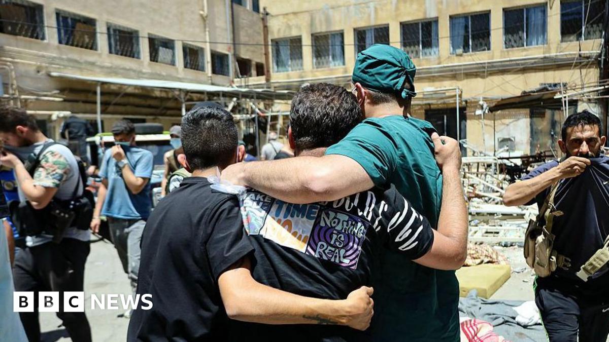 A health worker and other men walk in a hospital courtyard, past the bodies of victims of the recent clashes in Syria's southern city of Suweida on 17 July 2025