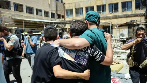AFP A health worker and other men walk in a hospital courtyard, past the bodies of victims of the recent clashes in Syria's southern city of Suweida on 17 July 2025