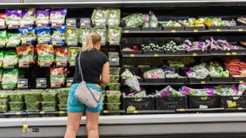 Getty Images Woman wearing a black T-shirt and blue shorts shopping in the fresh fruit and vegetable section of a US supermarket
