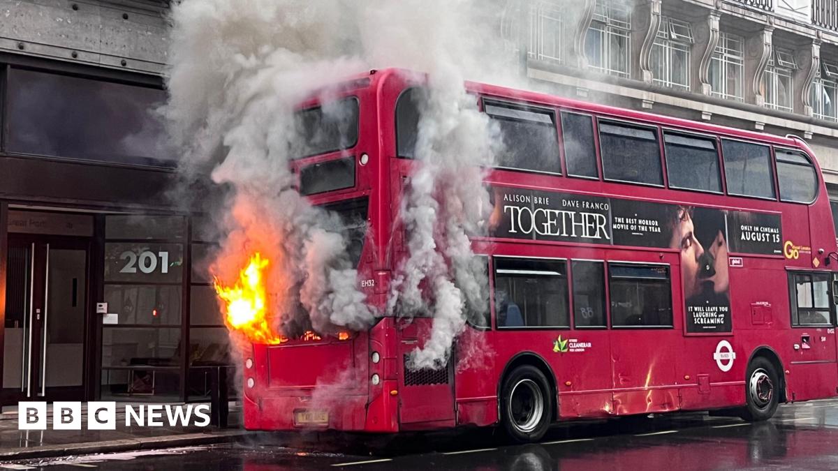 Red double decker bus with flames and smoke emerging from the rear