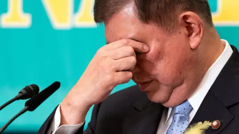 Getty Images Japan's Prime Minister Shigeru Ishiba runs his eyes while standing behind microphones, wearing a suit