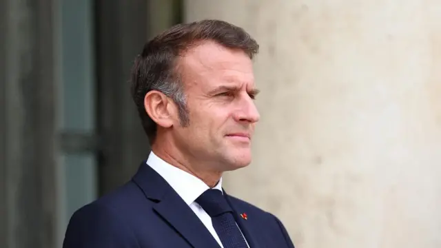 A file photo of Macron - he is seen from the side, wearing a suit and standing looking off camera