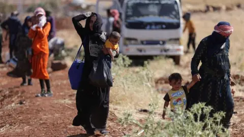 Reuters Bedouin women with children walk along a dirt path in southern Syria. One is holding the hand of a toddler, and another carries a baby in her arms