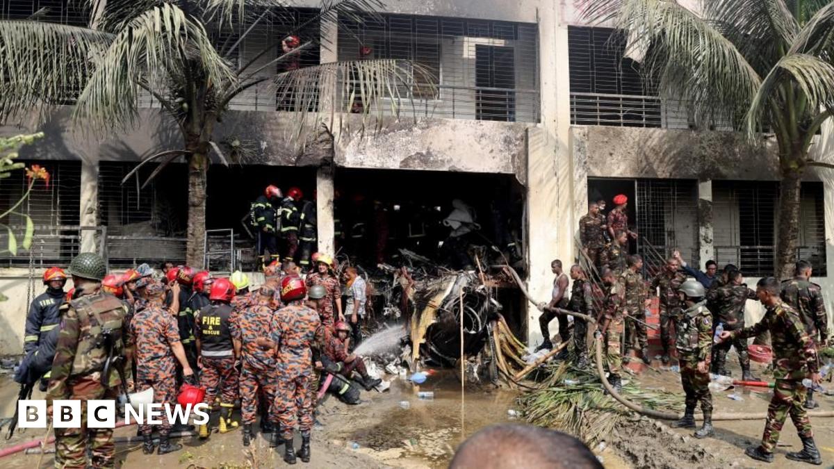 Crowds of people stand on the streets and on unfinished buildings looking down at an ambulance which makes its way through the crowd.