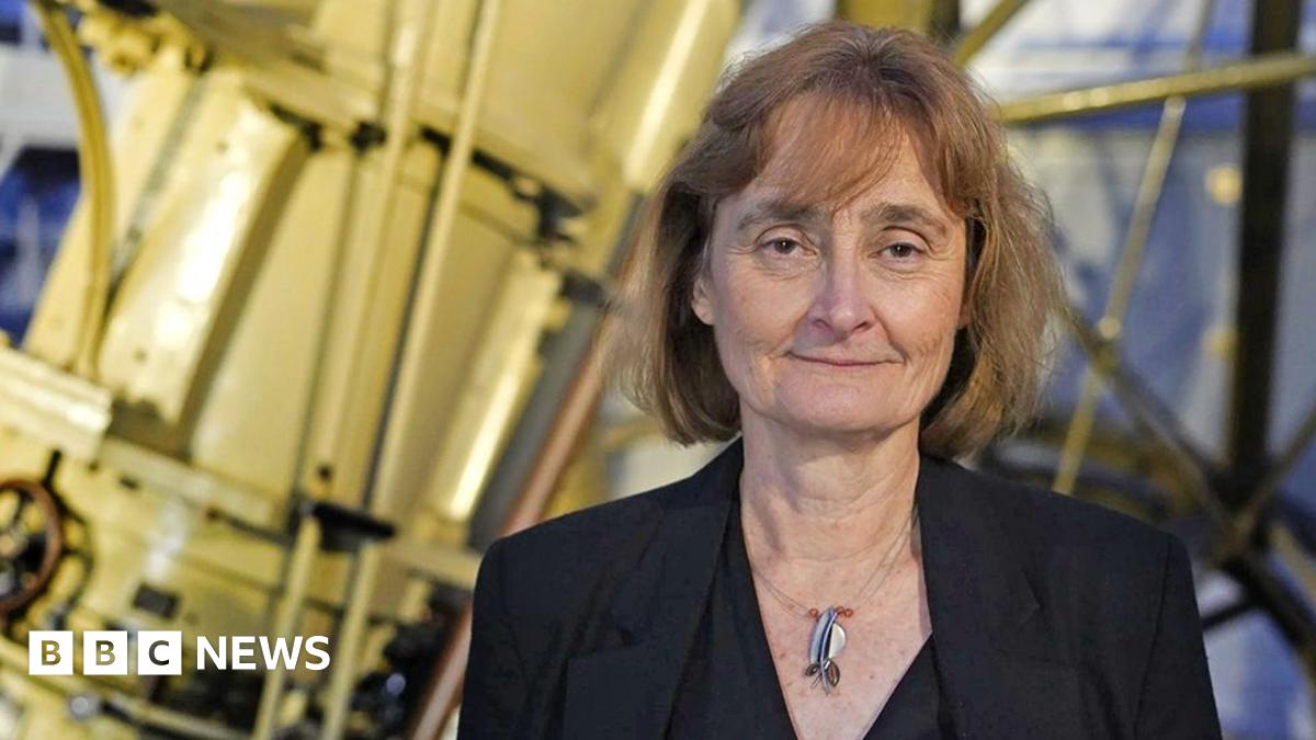 Michele Dougherty in smart black suit standing in front of telescope.