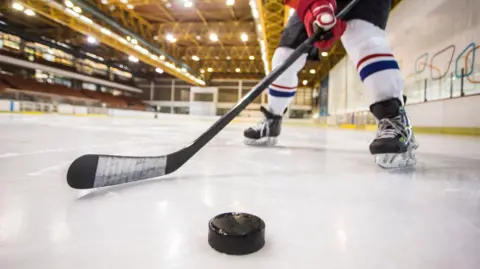 Getty Images An image of an unseen hockey player wearing a red glove and striped white, red and blue socks hitting a puck along the ice
