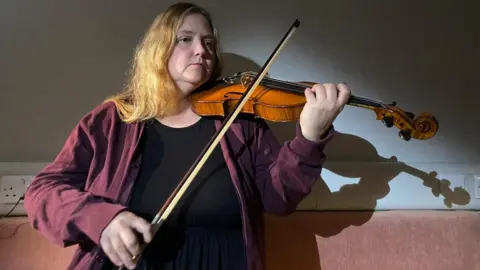Anna is playing the violin. The image shows her with the violin tucked under her chin and holding the bow in her hand. 