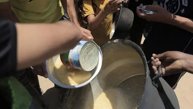 Palestinians including children use cans and bowls to take hot food from a large pot