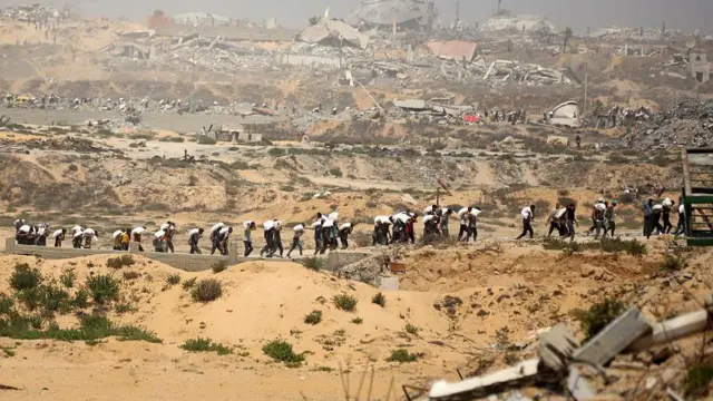 A long line of Palestinians carrying sacks of flour from aid trucks in northern Gaza on July 27
