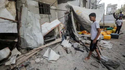 Reuters A Palestinian boy inspects the site of an Israeli strike that killed 10 Palestinians, including six children, who were queueing at a water distribution point, in Nuseirat refugee camp, central Gaza (13 July 2025)