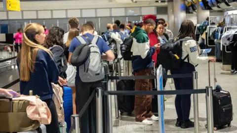 Getty Images People checking their phones while waiting in a busy queue at check in at Heathrow Airport 