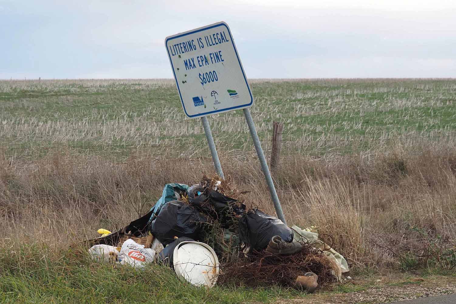 A pile of dumped rubbish under a sign warning of fines for littering. 