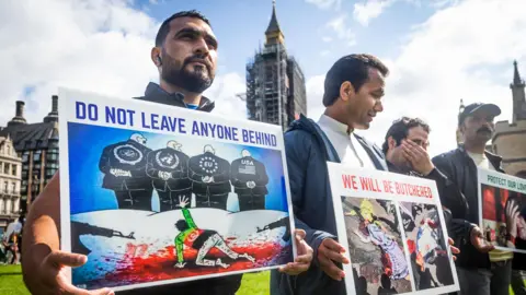 Getty Images Protesters in London hold placards calling for the safe evacuation of Afghans that had worked with the British military. The posters read: "Do not leave anyone behind". The image shows a man wearing a t-shirt with an Afghan flag on his knees in a pool of blood, grasping for help from four men who are looking the other way.