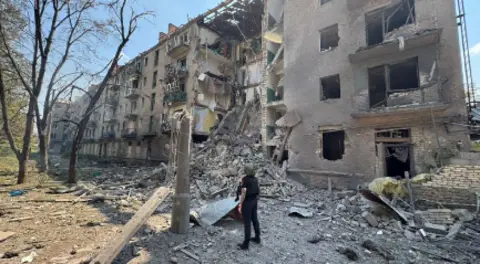 Donetsk Regional State Administration A person in a helmet stands looking at a damaged building