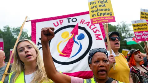 Reuters A crowd holds banners and signs, some of which read: "Stand up to Racism".