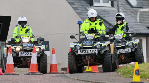 PA Media Three police officers on quad bikes with cones near them. They are wearing white helmets and hi-vis jackets