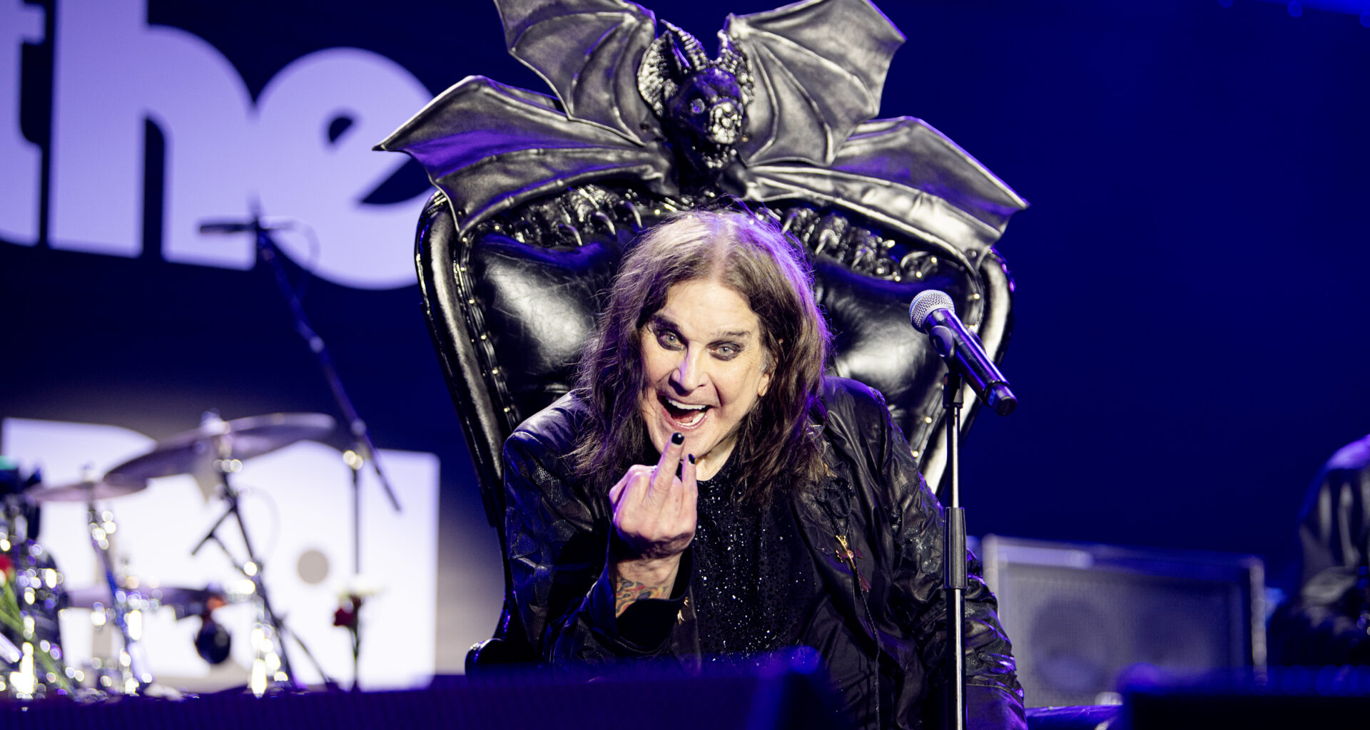 Ozzy Osbourne holding a finger up at the camera from his throne on stage