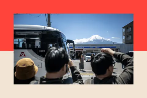AFP via Getty Images Tourists take pictures from the opposite street of a convenience store with Mount Fuji on 3 May 2024.
