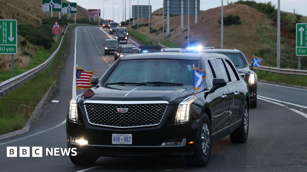 US President Donald Trump's motorcade on the A77 in Maybole, South Ayrshire, as arrives to begin his five-day private trip to the country. His black car is adorned with US and Scotland flags, and is followed by other black cars, all with their headlights on.