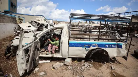 NurPhoto via Getty Images Displaced Palestinian children play inside a destroyed police car in a temporary camp within the site of the Arafat Police Academy, in the destroyed police camp affiliated with Hamas, in Gaza City (10 April 2025)