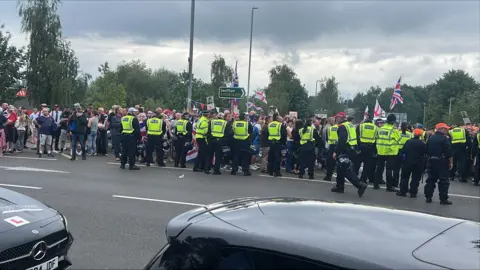 Richard Knights/BBC People waving flags and a line of police officers standing in front of them.