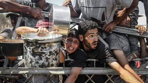 Anadolu via Getty Images Palestinians carrying pans gather to receive hot meals from a charity kitchen in Gaza City, northern Gaza (23 July 2025)