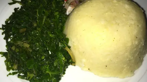 A white plate with boiled spring greens on the left and ugali (maize meal) on the right.