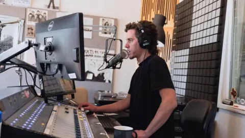 Travis Bubenik speaking into a microphone in a radio studio.