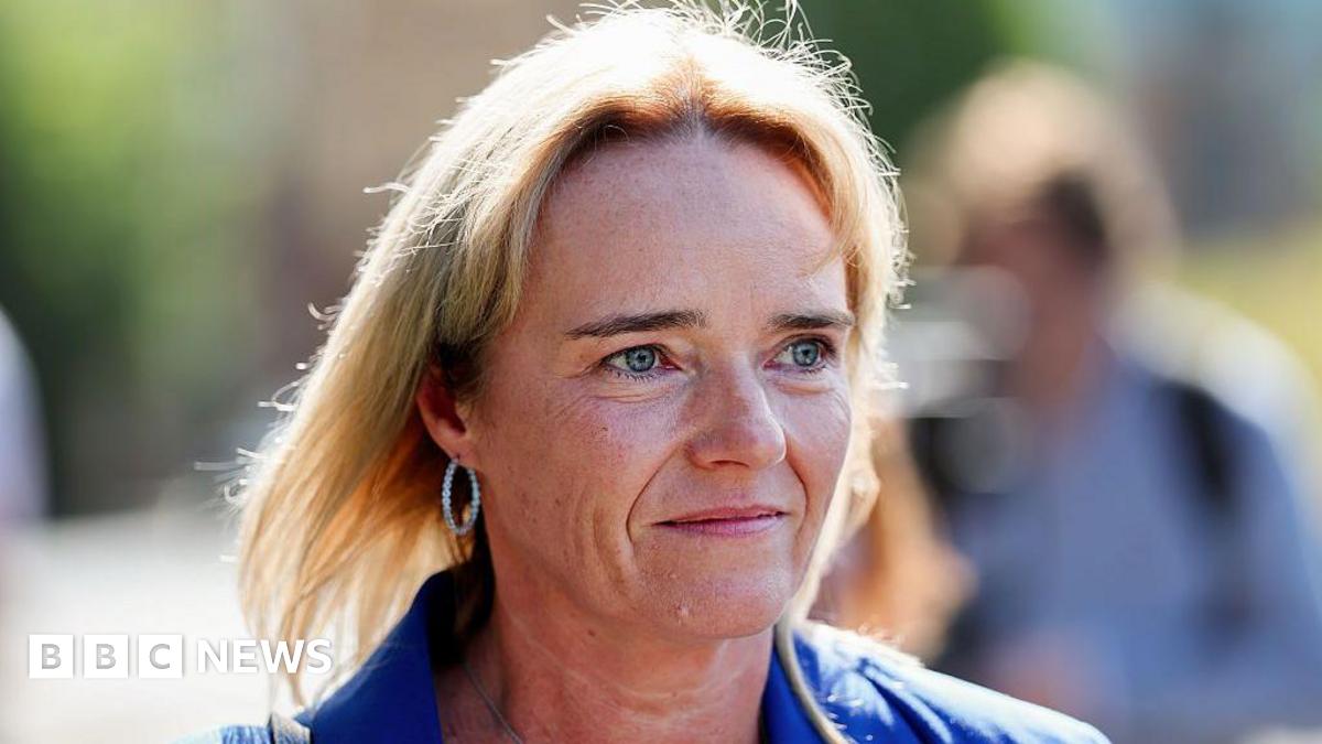 Sandie Peggie - a woman with blond hair to her shoulders and wearing a blue suit - smiles while walking outside