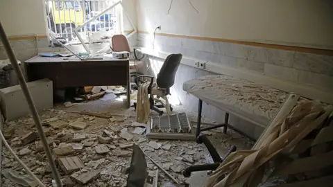 Fatemeh Bahrami/Anadolu via Getty Images A view of Evin prison is seen in the wake of an Israeli strikes on the site in June. A cot can be seen covered in debris, and rubble covers the floor. A barred window is seen with light shining through it. Wires hang from the walls and ceiling.