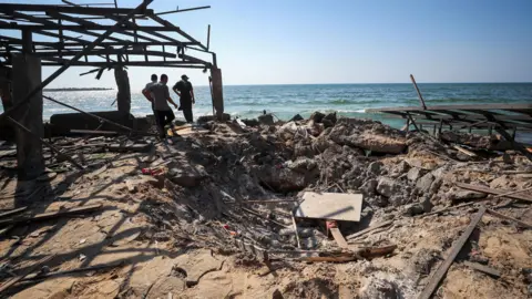 Reuters Three people inspect a crater next to the sea at the site of the Al-Baqa beach cafe in Gaza, after an Israeli air strike