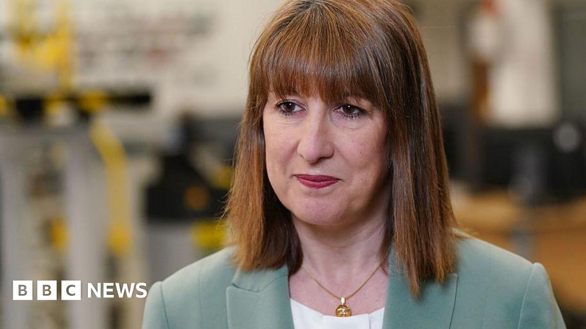 Chancellor Rachel Reeves wearing a light green jacket and white top standing in front of a blurred background