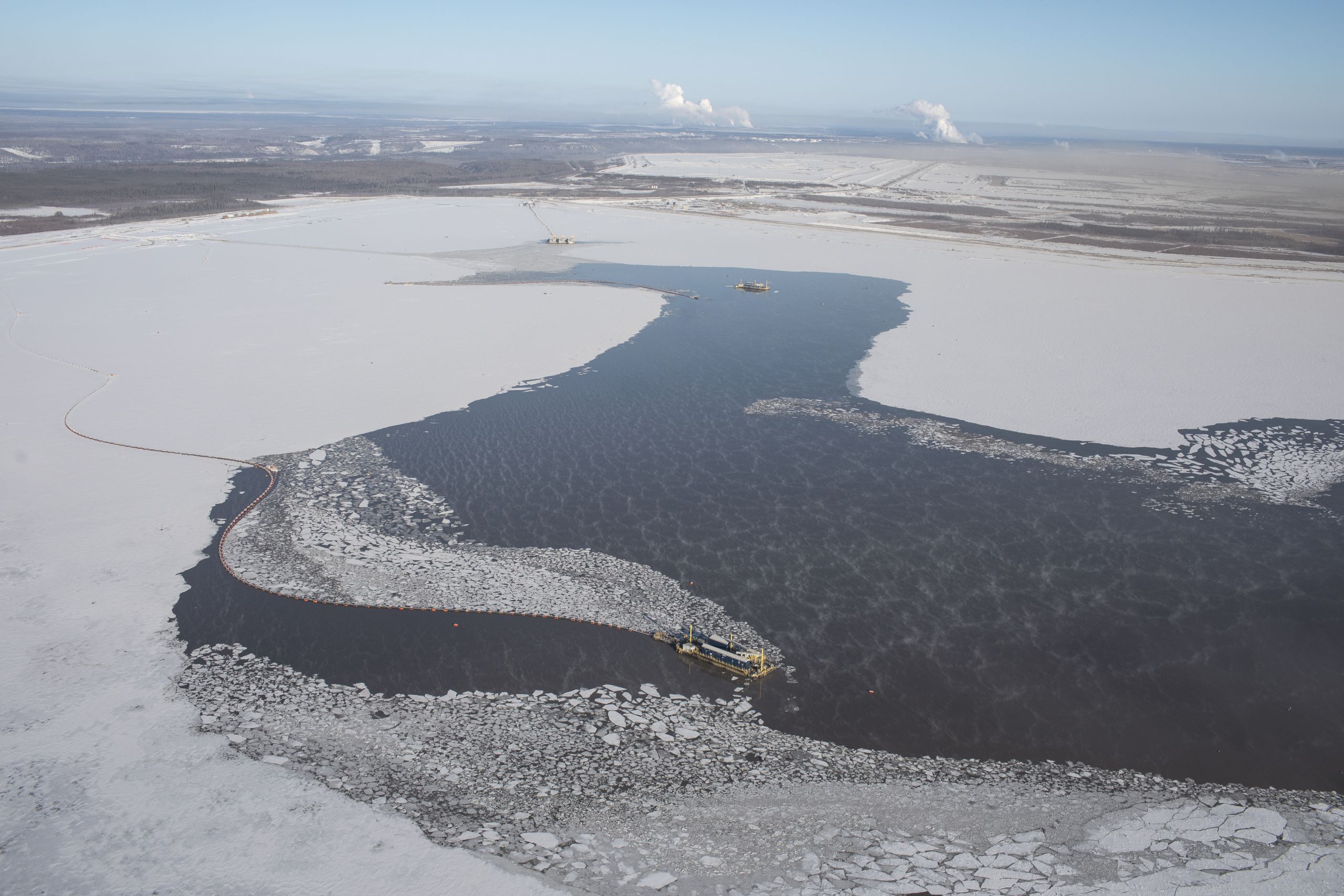 aerial shot of a flat plain covered in ice and snow with a dark liquid covering part of it