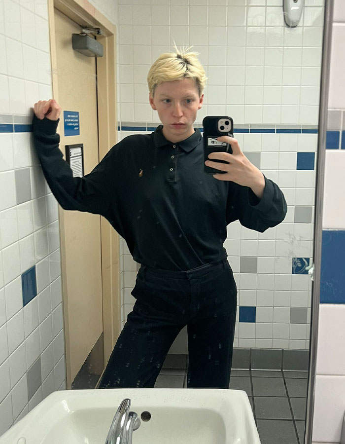 Young model taking a mirror selfie in a bathroom, reflecting on transition and detransition experiences.