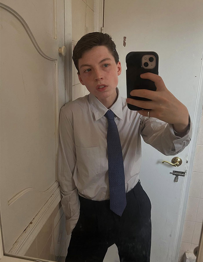 Model taking a mirror selfie wearing a shirt and tie, reflecting on detransition after transition at age 15.