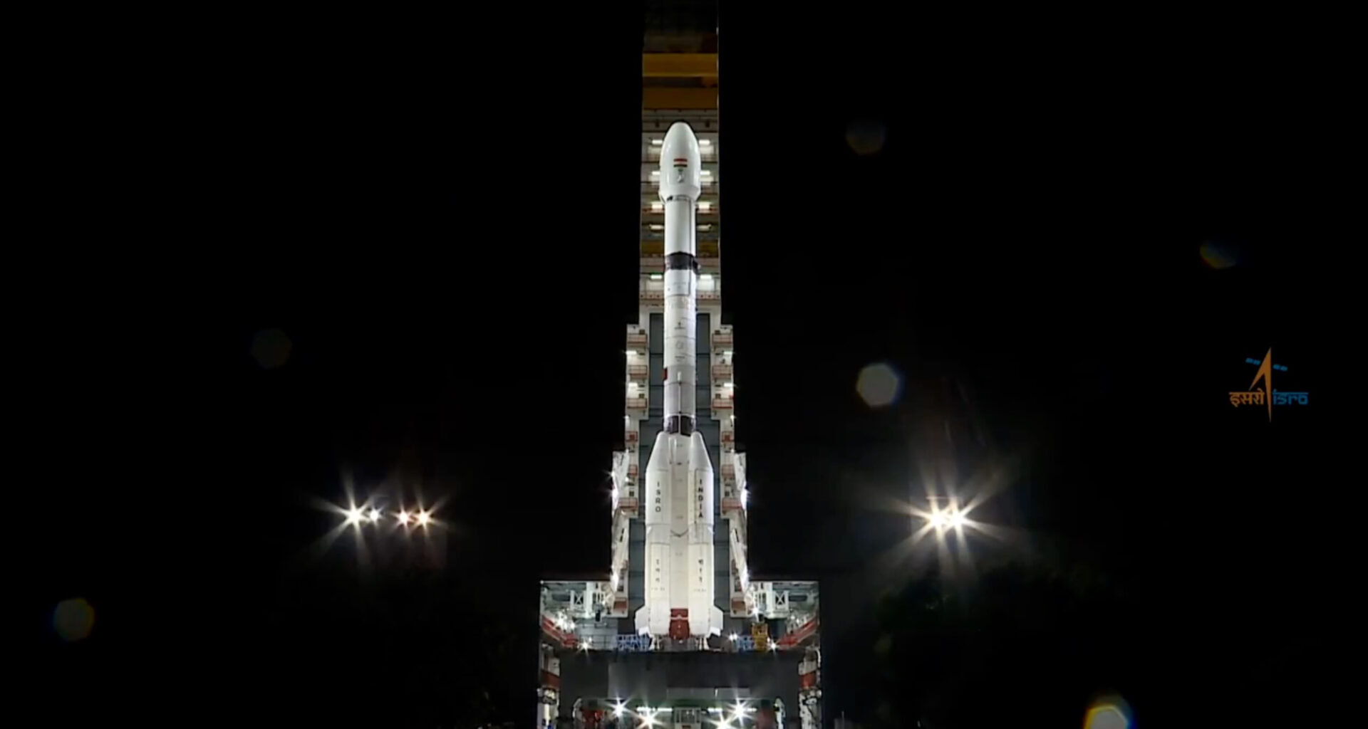 a large white rocket rolls out from its assembly hangar at night
