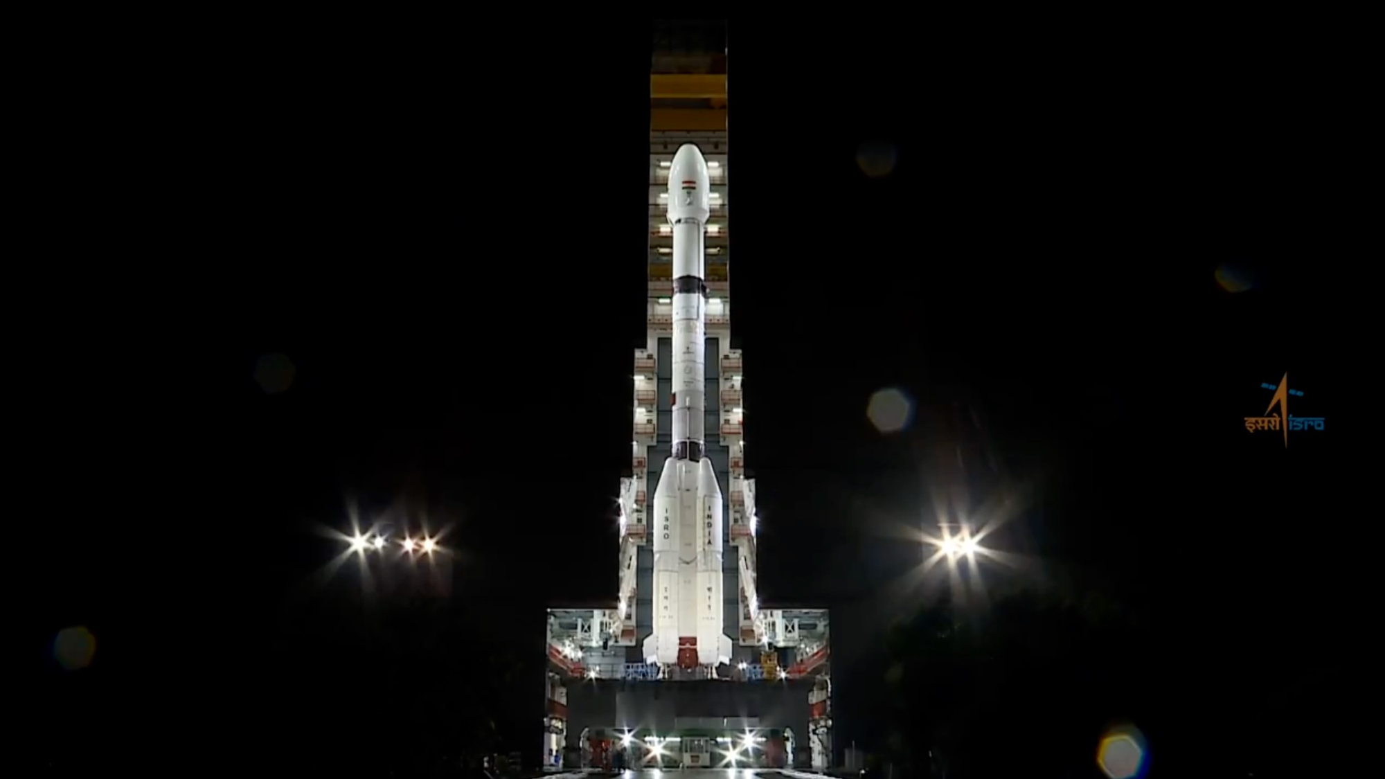 a large white rocket rolls out from its assembly hangar at night