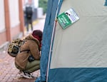 A person speaks to someone inside of a tent, camping on the sidewalk in downtown Portland, Ore., Nov. 15, 2023. 