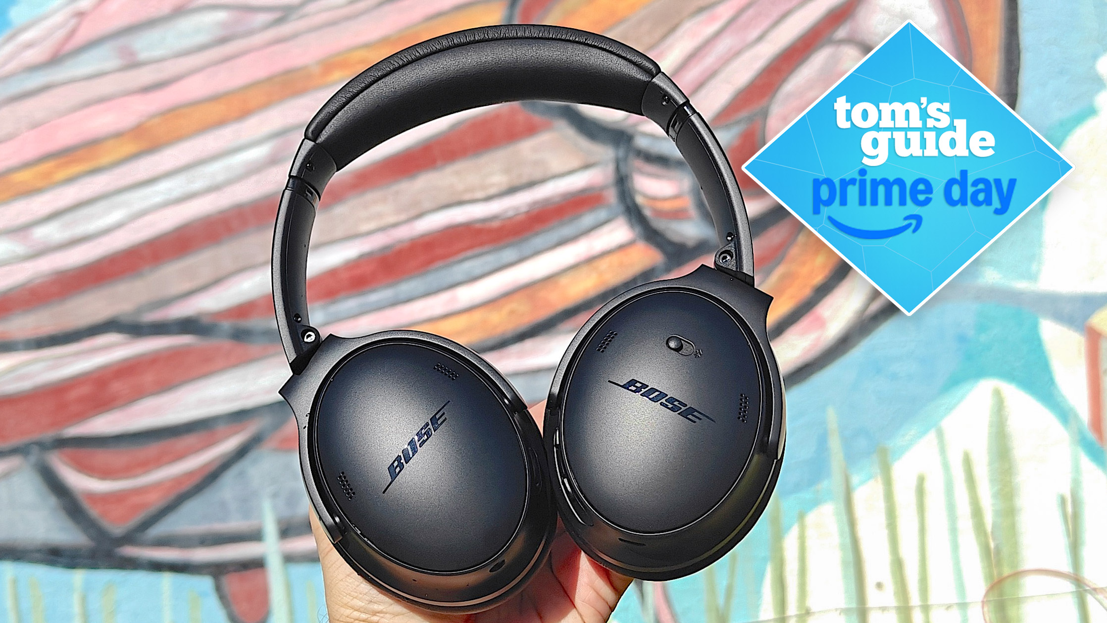 Bose Quiet Comfort headphones in a user's hand against a graffiti backdrop