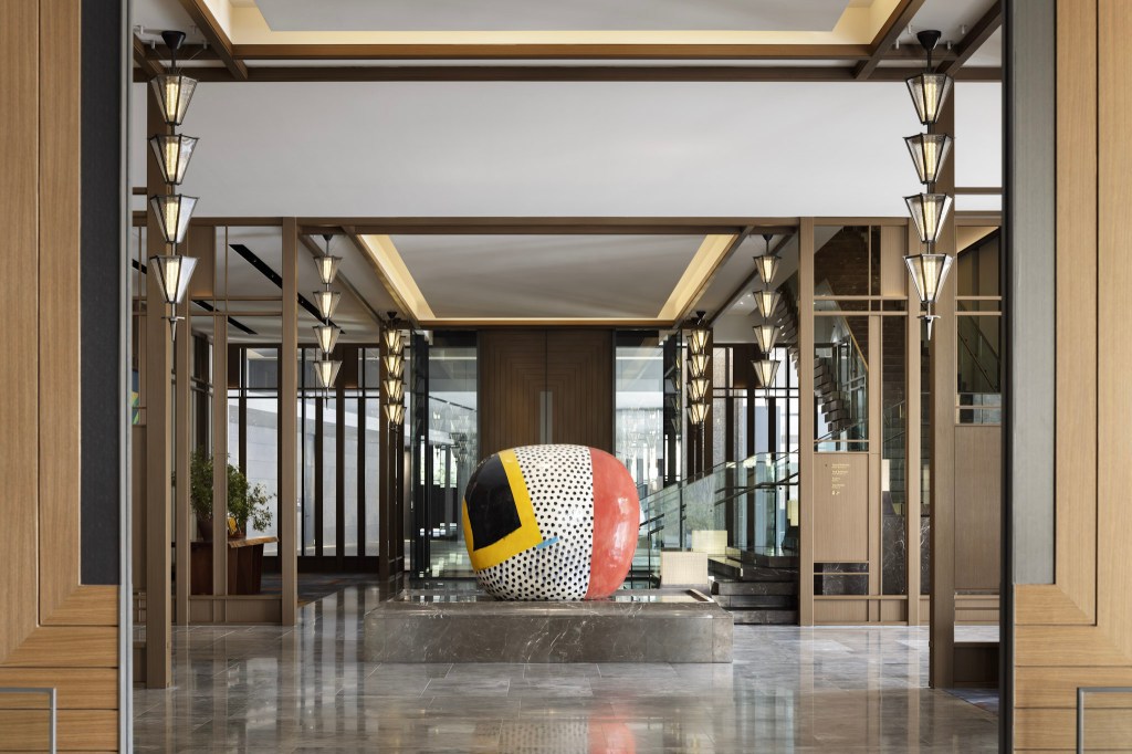 Elegant hotel entrance with modern lantern-style lighting and a bold abstract sculpture as the focal point in the lobby. Waldorf Astoria Osaka - Arrival. Hilton