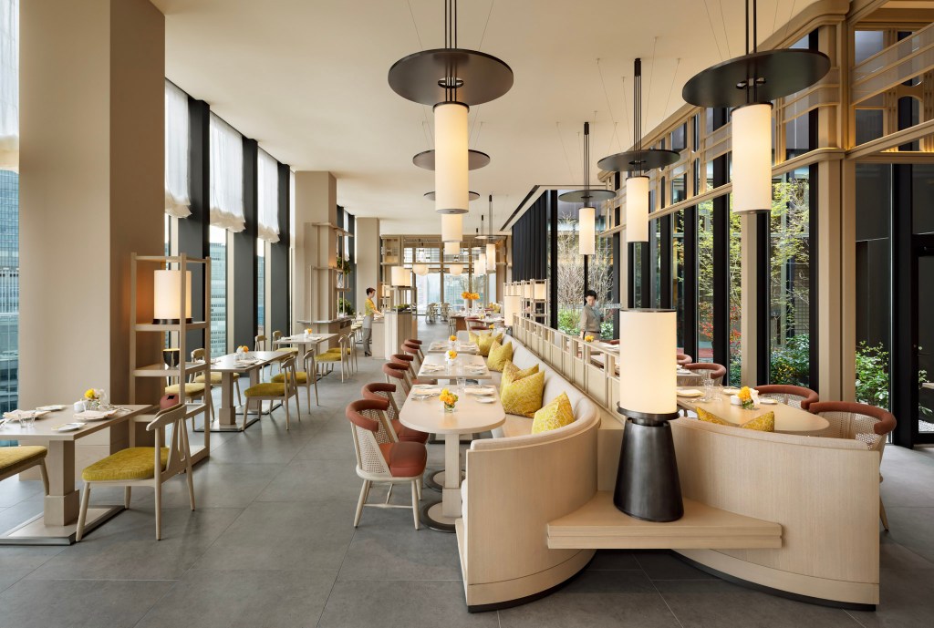 Bright and airy brasserie with floor-to-ceiling windows, neutral tones, and elegant modern dining furniture. Jolie Brasserie, Waldorf Astoria Osaka. Hilton