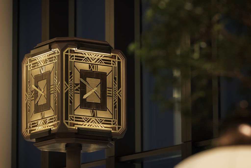 Close-up of an ornate, illuminated four-sided art deco-style clock with golden accents. Waldorf Astoria Osaka - Peacock Alley Clock. Hilton