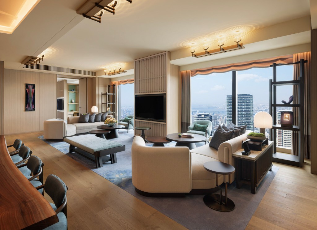 Spacious presidential suite living area with panoramic city views, modern furnishings, and warm wooden tones. Presidential Suite Living Room, Waldorf Astoria Osaka. Hilton