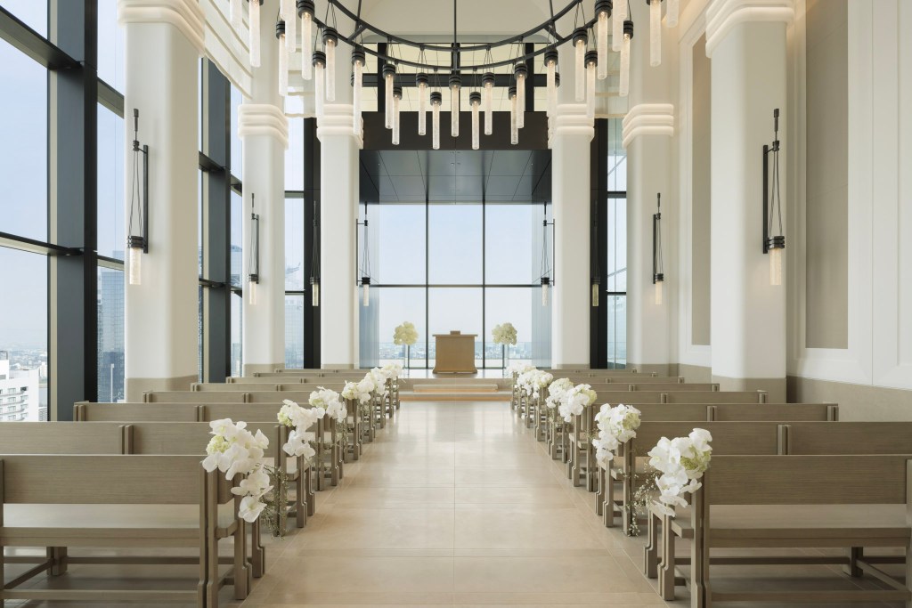 Modern wedding chapel with tall windows, elegant hanging lights, and floral decorations on wooden pews. The Chapel, Waldorf Astoria Osaka. Hilton