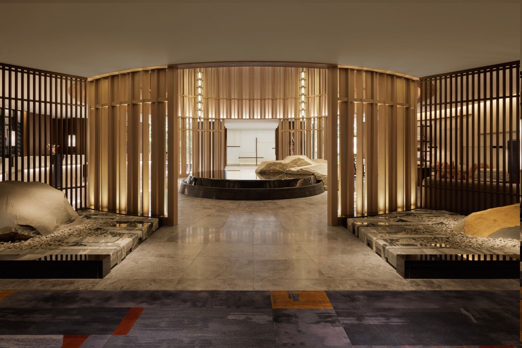 Zen-inspired lobby space with natural stone, wooden slat walls, and minimalist Japanese garden elements. Waldorf Astoria Osaka, The Lantern. Hilton