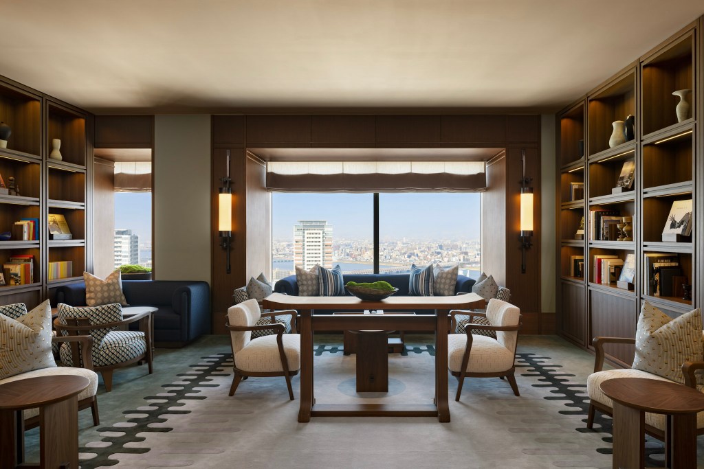 Sophisticated hotel library with built-in bookshelves, stylish seating, and a large window offering city skyline views. Waldorf Astoria Osaka - The Library. Hilton