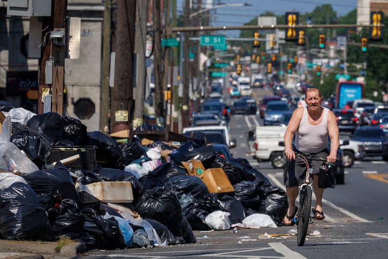 Cyclist riding beside large garbage dump along Allegheny Avenue at C Street during AFSCME District Council 33's strike.