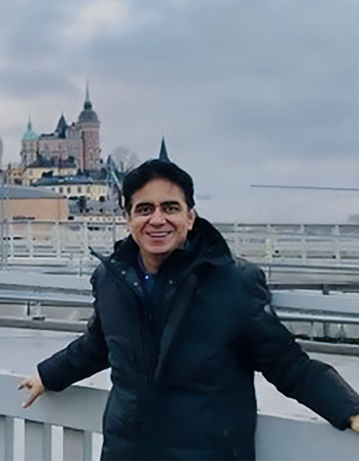 Man in a black winter jacket smiling outdoors near a railing with a castle in the background, related to Air India pilot news.